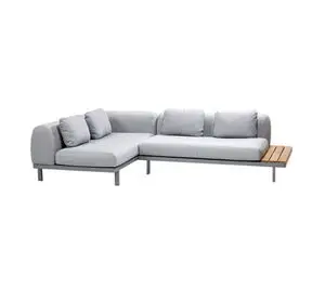 Lysegrå L-formet sofa med chaiselong til venstre og sidebord i træ til højre.